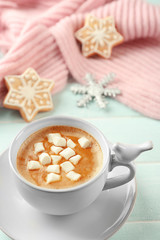 Cup of hot cacao with marshmallow, cookies and warm scarf on blue table