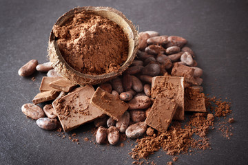 Bowl with aromatic cocoa beans and chocolate on grey background, close up