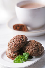Cup of cocoa with chocolate chip cookies and mint on light background