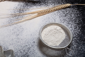 Wheat ears, baking forms, sieve and sprinkle flour on black back
