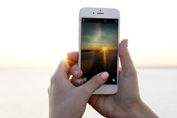 Female hands holding smart phone and taking photo of sunset