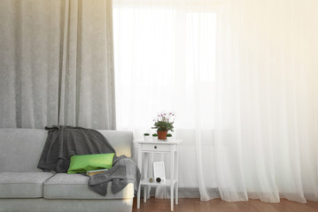 Grey sofa and small table with flowers on curtain background