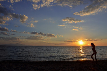 Fototapeta na wymiar silhouette of a young girl walking on beach with beautiful sunset behind her Siviri beach, Greece