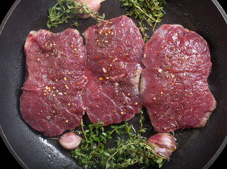 Fresh raw meat with thyme fried on black frying pan