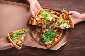People hands with sliced pizza on wooden table closeup