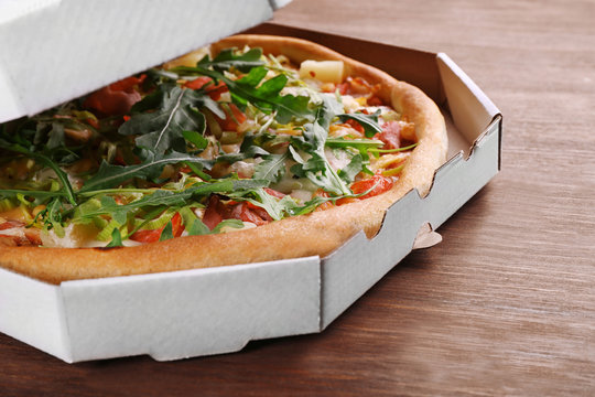 Fresh pizza in cardboard box on wooden table closeup