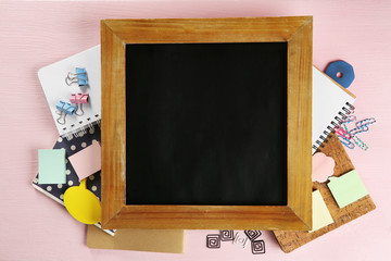 Small school blackboard with stationery on pink wooden background
