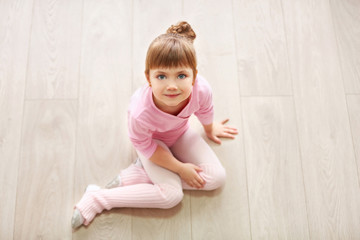Fototapeta premium Little cute girl in pink leotard sitting on floor at dance studio