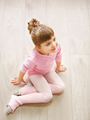 Little cute girl in pink leotard sitting on floor at dance studio