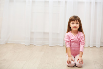 Little cute girl in pink leotard sitting on floor at dance studio