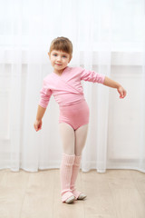 Little cute girl in pink leotard making new ballet movement at dance studio