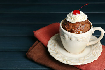Chocolate mug cake with cream and cranberry on dark wooden background