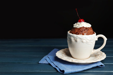 Chocolate mug cake with cream and cherry on a table in front of dark background