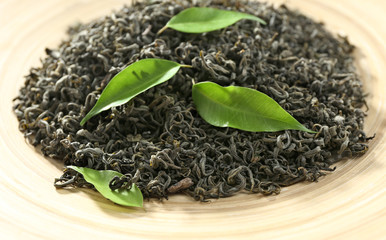Dry tea with green leaves in beige plate, closeup