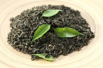 Dry tea with green leaves in beige plate, closeup