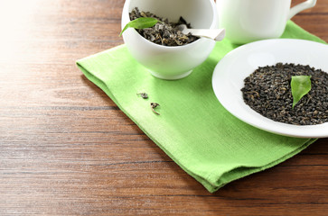 Dry tea with green leaves in plate and bowl on wooden table background
