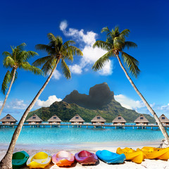  Otemanu  mountain, inclined palm trees over the sea and bright canoes on the beach. Island  Bora...