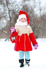 Little girl with Santa hat and red lantern in snowy park outdoor