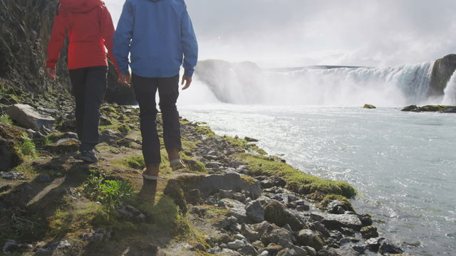 Couple visiting majestic Godafoss waterfall. Man and woman are on vacation at beautiful waterfall in Iceland. Male and female tourists are walking at famous attraction.