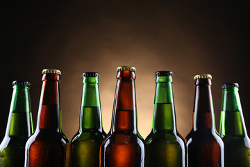Green and brown glass bottles of beer on dark lighted background, close up