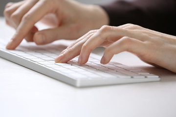 Female hands using keyboard on white wooden table, close up
