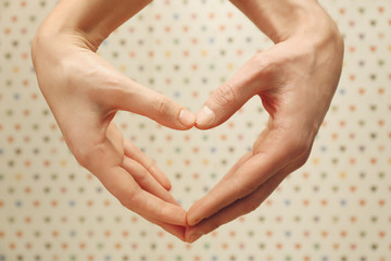 Male and female hands making heart with fingers on blurred background
