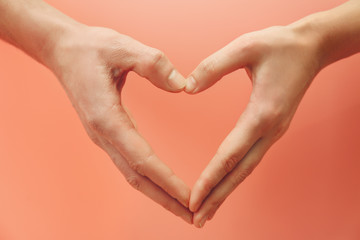 Male and female hands making heart with fingers on pink background