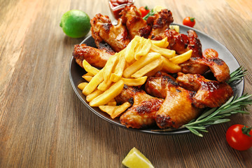Grilled chicken wings with French fries, garden-staff and tomatoes on plate