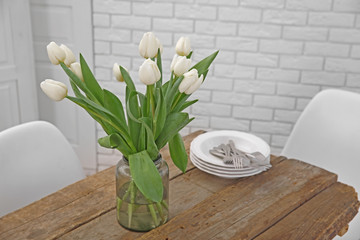 Beautiful bouquet of white tulips flowers and utensils on wooden table