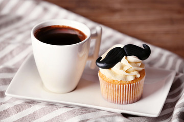 Cup of coffee and cupcake with mustache on napkin closeup