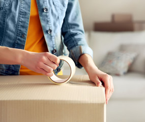 Young girl sealing with tape big cardboard box for moving
