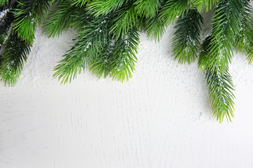 Snowy fir twigs on light wooden background