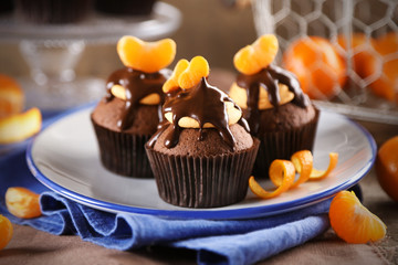 Three tasty cupcakes with slice of mandarin and chocolate on a plate over wooden background