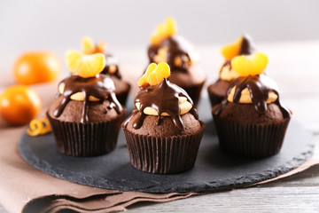 Tasty cupcakes with slice of mandarin and chocolate on slate plate over light wooden background