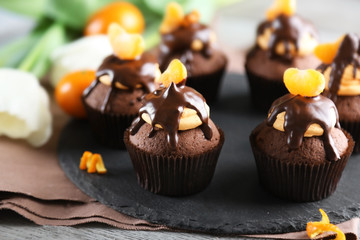 Tasty cupcakes with slice of mandarin and chocolate on slate plate, close up
