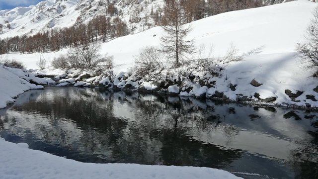 Winter mountain river and snowy hill reflection on water surface.
