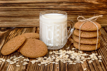 Oat cookies with glass of milk and oat flakes on wooden backgrou