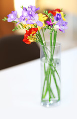 Beautiful bouquet of colorful freesias flowers on wooden table at living room
