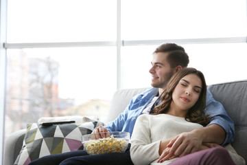 Young man watching TV and woman sleeping on his shoulder on a sofa at home