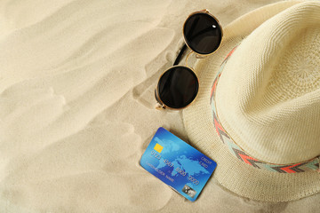 Bank card with male hat and sunglasses on sand background