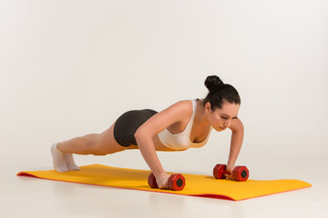 Strong young woman doing push ups exercise with dumbbells. 