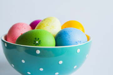 Colorful easter eggs in green spotted bowl on light background