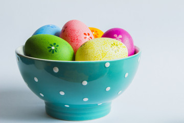 Colorful easter eggs in green spotted bowl on light background
