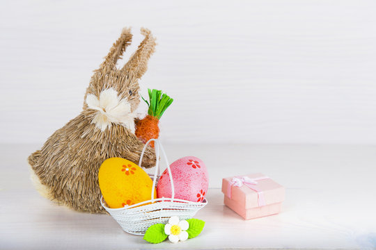 Wicker Easter bunny with Easter eggs in basket on white wooden b