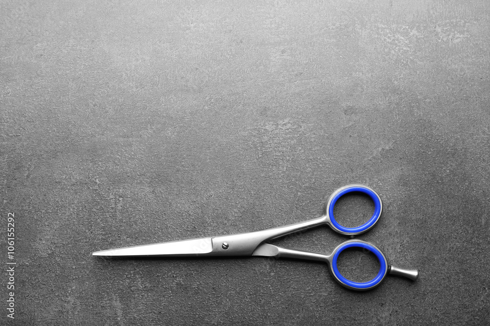 Wall mural Professional metal scissors with blue-colored handle on a dark grey surface with copy space, top view