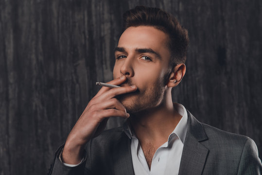Handome brutal man in suit on the grey background smoking a ciga