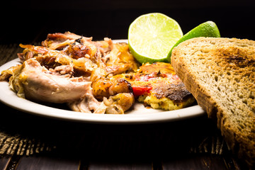 Roasted pork meat, limes and scrambled eggs with red papers and slices of bread 