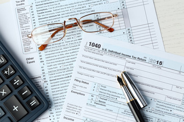 1040 Individual Income Tax Return Form for 2015 year with a pen to fill, calculator and metal rimmed glasses, close up