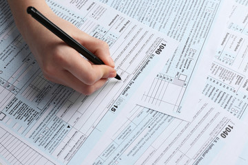 Female hand holding a black pen and filling in the 1040 Individual Income Tax Return Form for 2015 year on the white desk, close up