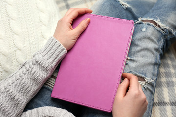 Young woman sitting on the sofa  with white cushion and holding a purple notebook on her knees, close up